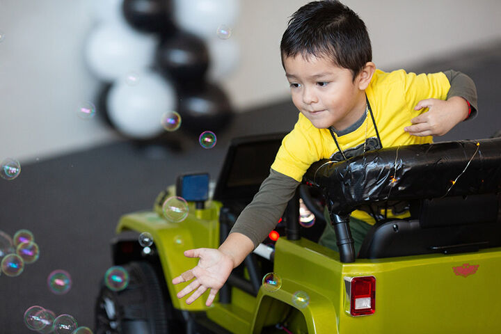 Toddler riding a toy truck and playing with bubbles.